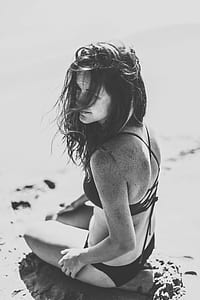 grayscale photography of woman wearing bikini sitting on sand at daytime thumbnail