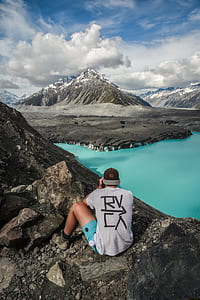 man wearing white shirt sitting on black hill during daytime thumbnail