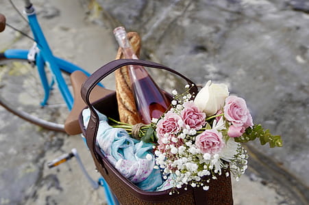 pink rose flowers and glass bottle inside brown wicker basket on blue bike thumbnail