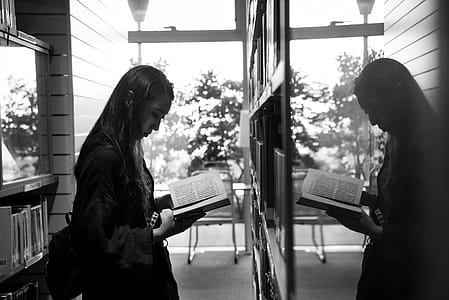Greyscale Photo of Girl Reading a Book Reflecting on a Glass thumbnail