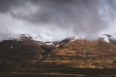 photo of brown mountain with snow on top under cloudy sky thumbnail