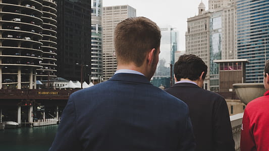 man wearing black suit facing two men walking towards him thumbnail