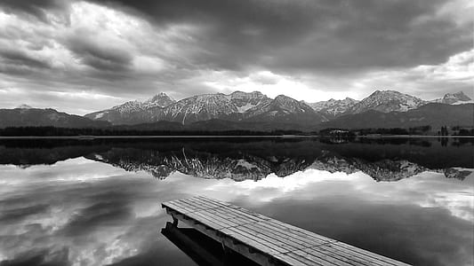 grayscale photo of dock on body of water under cloudy sky thumbnail