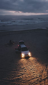 silver SUV with lighted headlight parked on beach side thumbnail
