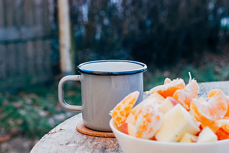 slice orange fruit in white bowl beside grey mug thumbnail