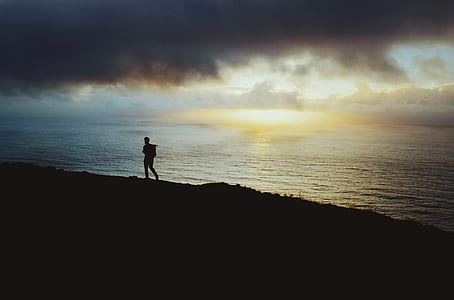 silhouette of man walking on sand near body of water thumbnail