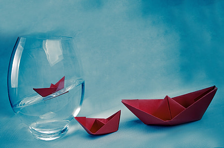 two red origami boats beside clear glass fish bowl filled with water thumbnail