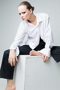 close up photograph of woman in white dress shirt and black pants sitting on cube box thumbnail