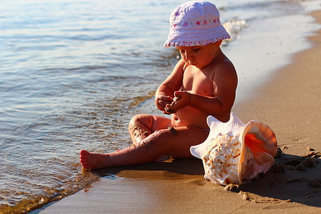 baby wearing white hat beside conch shell thumbnail