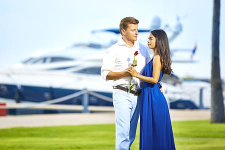 man facing woman while holding red flower with yacht background thumbnail