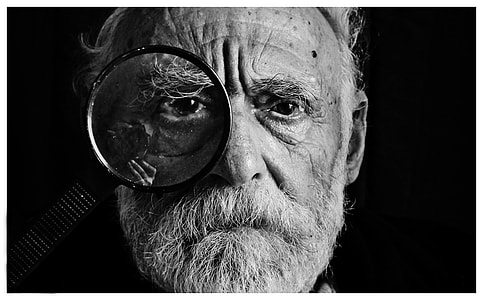 grayscale shot of man with magnifying glass on his right eye thumbnail