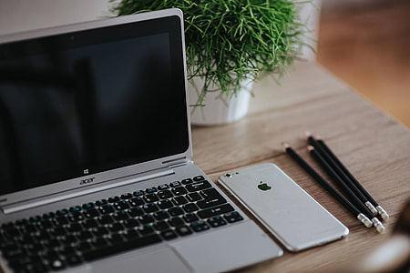 Silver Acer laptop on a wooden desk with a green plant, pencils and an Apple iPhone thumbnail