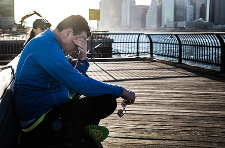 man sits on brown bench while holding eyeglasses thumbnail