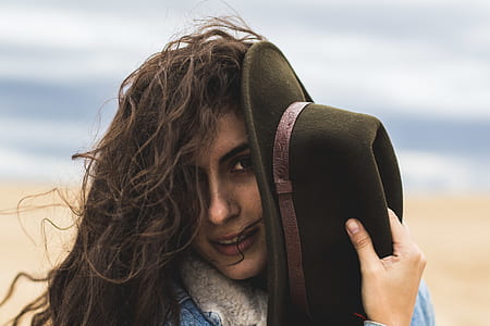 shallow focus photography of woman covering her left face with hat thumbnail