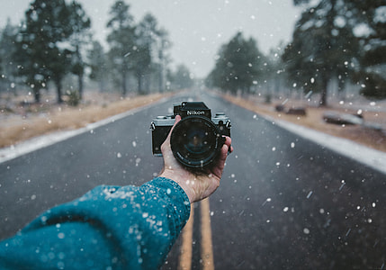 person holding Nikon camera on road over pouring snow thumbnail