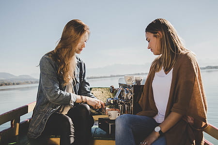 two women sitting beside espresso machine overlooking body of water during daytime thumbnail