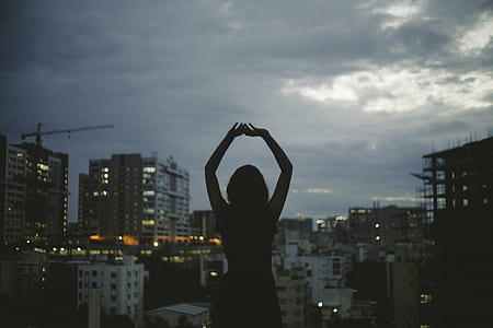 landscape silhouette photography of woman raising hands in front of buildings thumbnail