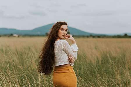 woman wearing white sheer long-sleeved crop top and yellow bodycon skirt standing in middle of grass field thumbnail