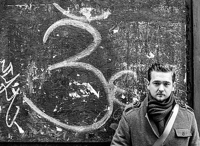 grayscale photo of man wearing coat behind wall thumbnail