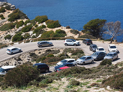 assorted-color vehicle lot traveling on road near sea during daytime thumbnail