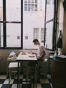 Man Sitting in Front of Table Holding Smartphone Beside Window thumbnail