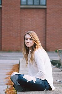 woman in white top and blue jeans sitting on gray concrete surface thumbnail