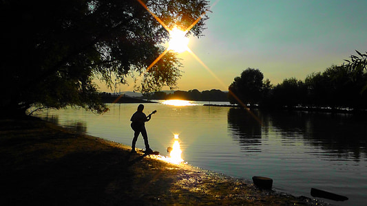 silhouette of person holding guitar standing beside seashore thumbnail