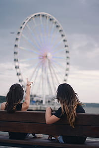 two women in black top sitting on wooden bench fronting ferris wheel thumbnail