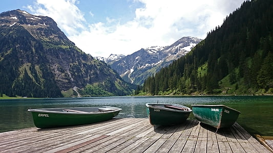 three green canoe boats on brown wooden dock beside body of water near mountains thumbnail