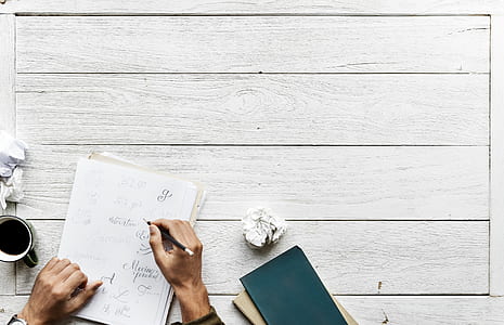 person writing on white paper beside mug thumbnail