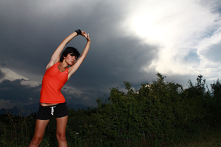 woman stretching body near trees under dark cloudy sky thumbnail