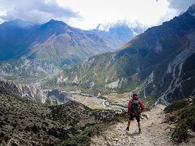 man standing on top of rocky cliff facing green filled mountains thumbnail