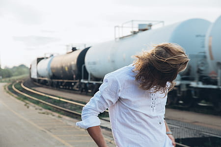 A long haired young caucasian man standing near passing train thumbnail