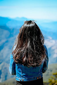 woman wearing blue denim jacket facing mountain range during day thumbnail