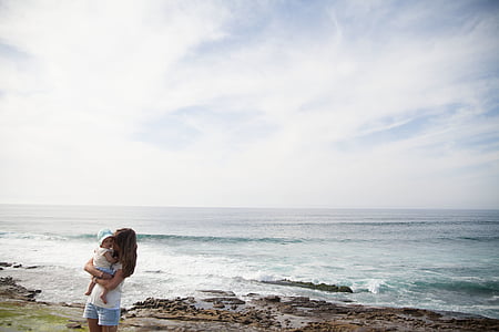 woman carrying baby near body of water during daytime thumbnail