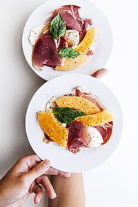 person holding two round white ceramic plates filled with raw meats thumbnail