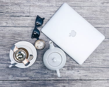 high angle photo of silver MacBook, white ceramic teapot, black Ray-Ban sunglasses, and a cup of coffee on brown wooden board thumbnail