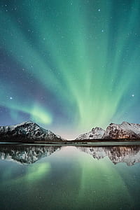 body of water between mountain under green sky thumbnail