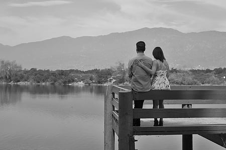 couple sitting on fence near body of water thumbnail