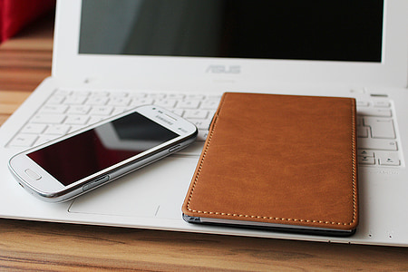 turned off white Samsung Android smartphone beside brown leather notebook on top of white turned off Asus laptop thumbnail