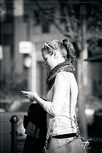 grayscale photography of a woman wearing sweatshirt and scarf walking on street while looking at her phone thumbnail