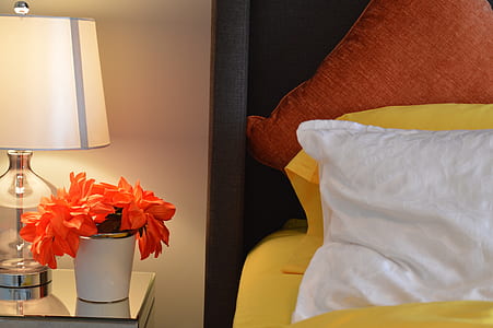orange petaled flowers with white ceramic pot near bed with white pillow thumbnail