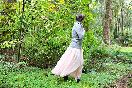 woman in gray jacket walking beside green leafed trees thumbnail
