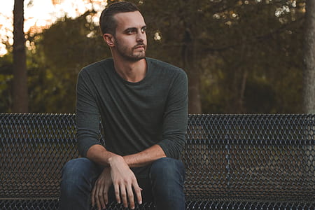 man sitting on black metal bench looking on his left side thumbnail