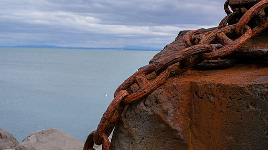 large rusty chains on stone overlooking sea during day thumbnail