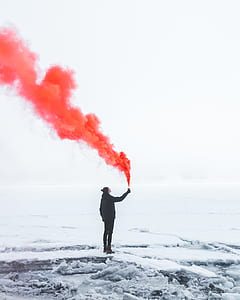 person in black jacket standing on snowy field while holding container with orange smoke thumbnail