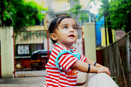 shallow focus photography of toddler in white and red striped shirt holding on rail during daytime thumbnail