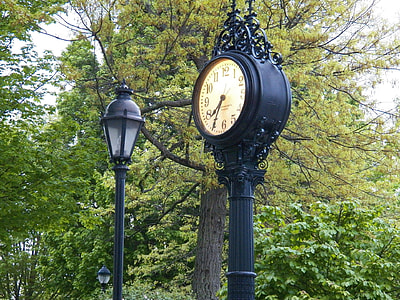 black metal analog pedestal clock near tree thumbnail