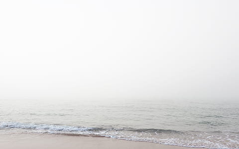 calm ocean waves on shoreline under white sky thumbnail
