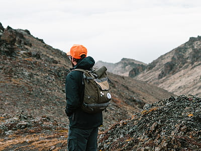 man carrying backpack while facing mountains thumbnail
